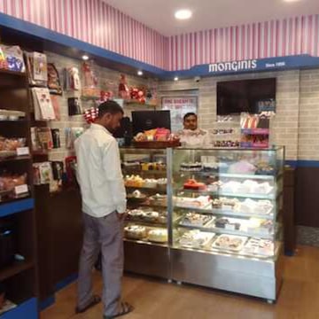 Customer at a glass cake display counter inside a Monginis shop